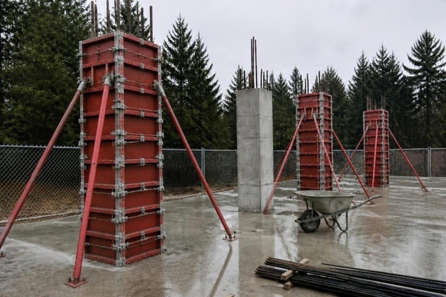 Red steel column forms with corner clamps and pipe braces on a concrete slab